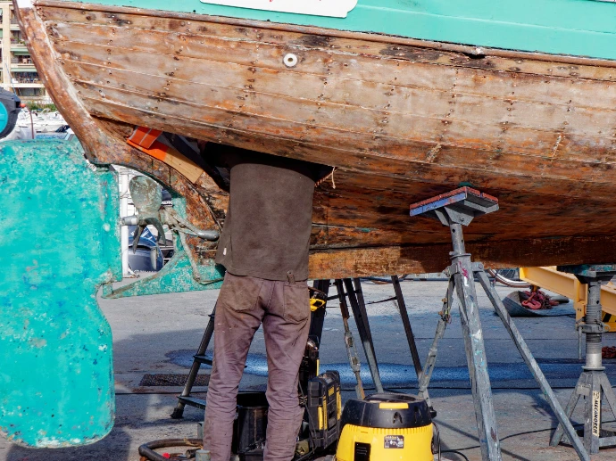 A person working under a wooden boat on stands